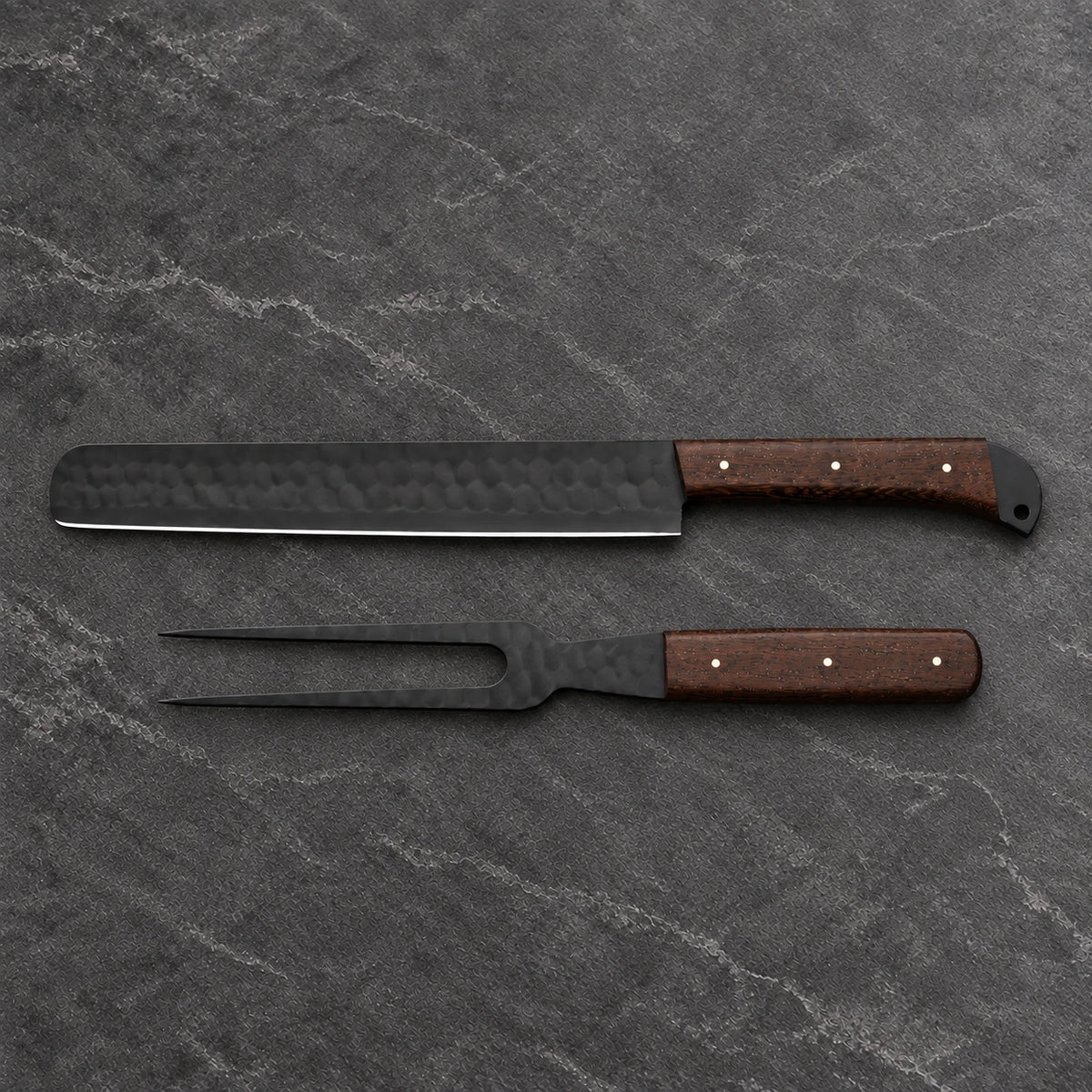 Black hammered brisket slicer and two-tine carving fork with wenge handles on dark stone