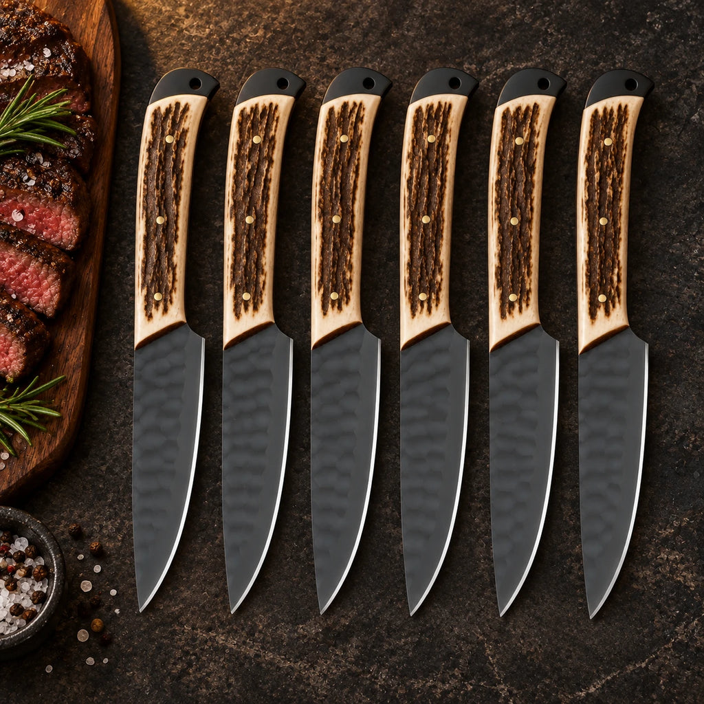 Set of 6 black hammered steak knives with stag handles beside sliced steak