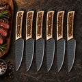 Set of 6 black hammered steak knives with stag handles beside sliced steak